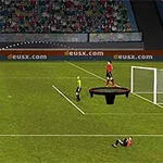 Bir futbol sahasında, kaleye doğru top süren bir oyuncu, hakem ve kaleye yakın bir zıplama platformunda duran oyuncu